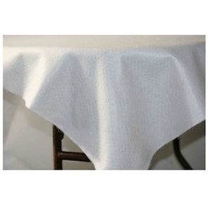 May include: A white tablecloth made of a soft, textured fabric. The tablecloth is draped over a table with a dark wooden frame.