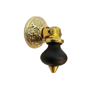 May include: A gold-toned doorstop with an ornate design and a black rubber base. The doorstop has a pointed tip and a swiveling joint.