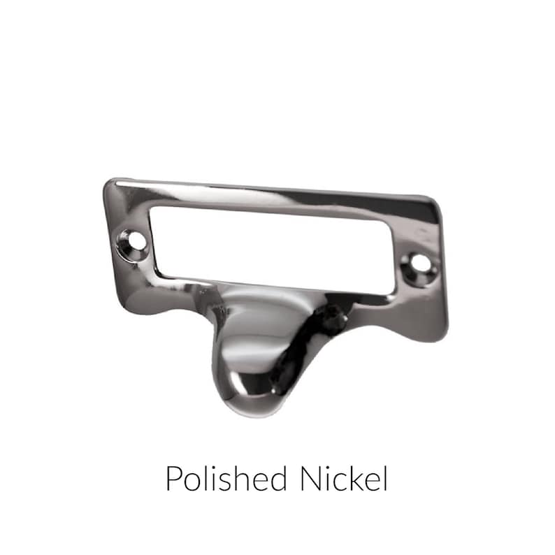 May include: A polished nickel drawer pull with a rectangular label holder. The pull has a rounded, teardrop-shaped handle.