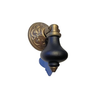May include: An antique-style cabinet pull with a black wooden handle and brass detailing. The pull has a decorative brass backplate and a conical tip. Suitable for drawers and cabinets.