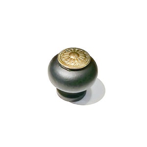 May include: Black cabinet knob with a gold decorative top. The top has a floral design.