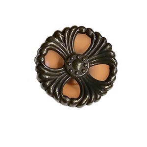 May include: A decorative, bronze-colored cabinet knob with a floral design. The knob features a central circular element surrounded by four petal-shaped cutouts, with a light orange color visible through the cutouts. The edges have a detailed, textured pattern.
