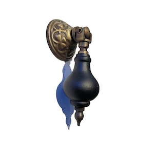 May include: A black and brass cabinet knob with a decorative floral design. The knob has a round base and a pointed tip.