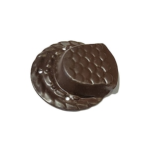 May include: A dark brown, decorative metal plate with a textured surface and a curved, raised section. The plate has a series of small holes around the edge and a detailed, embossed pattern. The object is set against a white background.