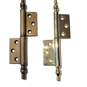 May include: Two decorative door hinges with a traditional design. The hinge on the left is a brass finish, while the hinge on the right is a polished brass finish.