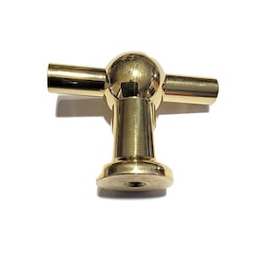 May include: A gold-toned T-shaped cabinet knob with a round, smooth top and a base with a threaded hole.
