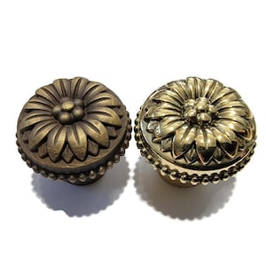 May include: Two decorative cabinet knobs with a floral design. One knob is gold and the other is a darker bronze color.