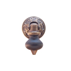 May include: A decorative cabinet knob with a round, ornate brass base and a dark wood knob.