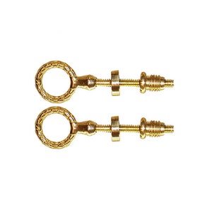 May include: Two gold-colored, ornate screw-in cabinet pulls. Each pull features a circular handle with a textured design, connected to a threaded rod with a decorative nut and screw end. The hardware is designed for installation on furniture.
