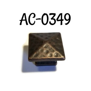 May include: A square-shaped, hammered, bronze-colored cabinet knob with a pyramid-shaped top. The knob is labeled "AC-0349".