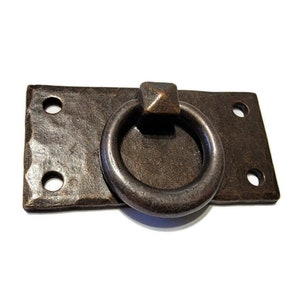 May include: A rustic, rectangular metal pull with a square ring handle. The pull has a dark brown finish and four holes for mounting.
