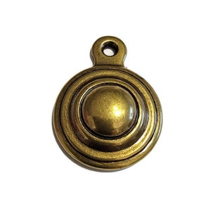 May include: A gold-toned metal pendant with a circular design. The pendant has a raised center and concentric circles around the edge.