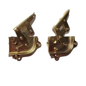 May include: Two gold-colored, folding hinges. Each hinge has a rectangular base with rounded corners and multiple screw holes. The hinges are designed to fold and have several moving parts, suggesting they are for furniture or cabinet doors.