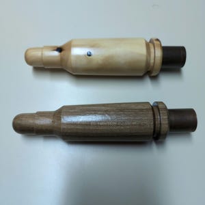 May include: Two wooden duck calls, one with a light wood finish and one with a dark wood finish. Both calls have a brass end cap.
