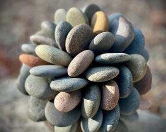 Può includere: Una sfera fatta di pietre lisce grigie, marroni e beige. Le pietre sono disposte a forma di fiore.