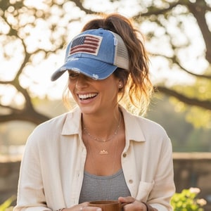Op de afbeelding: Een blauwe denim baseballcap met een distressed look, met een patch van de Amerikaanse vlag. De cap heeft een mesh achterkant en een gebogen klep. De hoed wordt door een persoon gedragen.