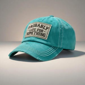 May include: Teal baseball cap with a curved brim and white stitching. The cap features a rectangular patch with the words "PROBABLY - LATE FOR - SOMETHING" in black text. The cap has a distressed look.