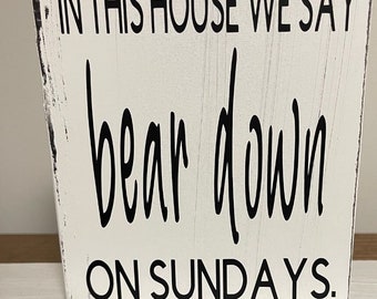 May include: White wooden sign with black text that reads "In this house we say bear down on Sundays."