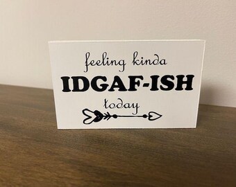 May include: White sign with black text that reads "feeling kinda IDGAF-ISH today" with a black arrow with heart shapes at each end.