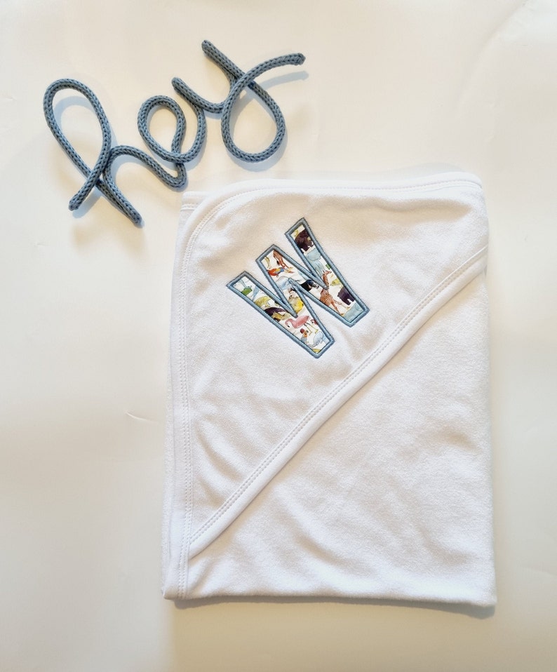 May include: White hooded towel with a large embroidered letter W. The letter is filled with a colorful pattern of animals.