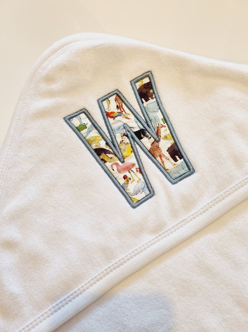 May include: White hooded towel with a blue outlined letter W embroidered on the front. The letter W is filled with a colorful pattern of animals.