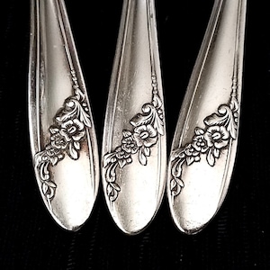 May include: Three silver spoons with ornate floral designs on the handles.