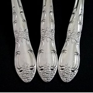 May include: Three silver forks with ornate handles. The handles have a floral design.