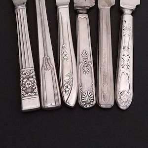May include: Six silver butter knives with ornate handles. The knives have a polished finish and intricate floral designs.
