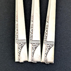 May include: Three silver forks with an ornate floral design. The forks are arranged side by side, with the handles pointing to the right.