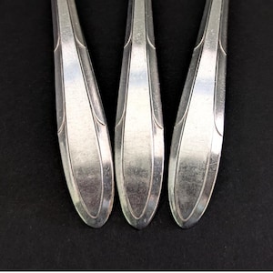 May include: Close-up of three silver spoons with a classic design. The spoons have a teardrop-shaped bowl and a decorative handle. The spoons are arranged vertically against a black background, showcasing their polished surfaces.