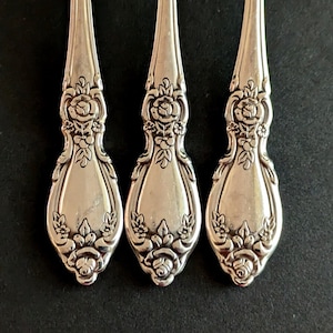 May include: Three silver-plated teaspoons with ornate floral designs. The spoons have a rounded bowl and a long, slender handle with a decorative floral pattern.
