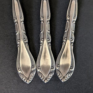 May include: Three silver forks with ornate handles. The handles have a decorative design with a pointed tip.