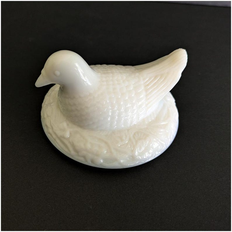 Puede incluir: Figura de paloma de cer&aacute;mica blanca en un nido. La paloma presenta texturas de plumas detalladas y un acabado liso y brillante. El nido tiene un aspecto texturizado y tejido. Adecuado para la decoraci&oacute;n del hogar.