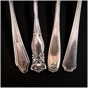 May include: Four silver spoons with ornate handles. The spoons have different designs on the handles, including a ribbon, a floral design, and a crown.