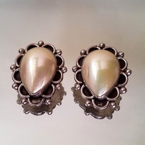 May include: A pair of silver earrings with a pearlescent white teardrop-shaped stone set in a silver filigree design.