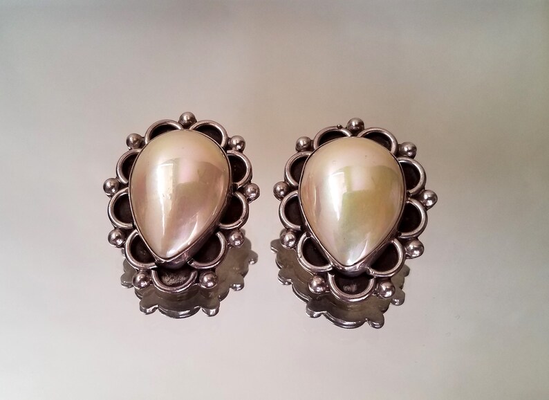 May include: A pair of silver earrings with a pearlescent white teardrop-shaped stone set in a silver filigree design.