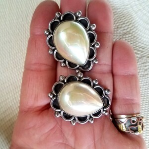May include: A pair of silver earrings with pearlescent white stones set in a decorative silver frame.