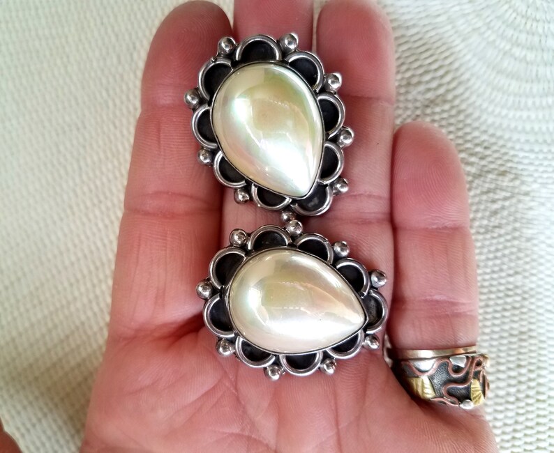 May include: A pair of silver earrings with pearlescent white stones set in a decorative silver frame.