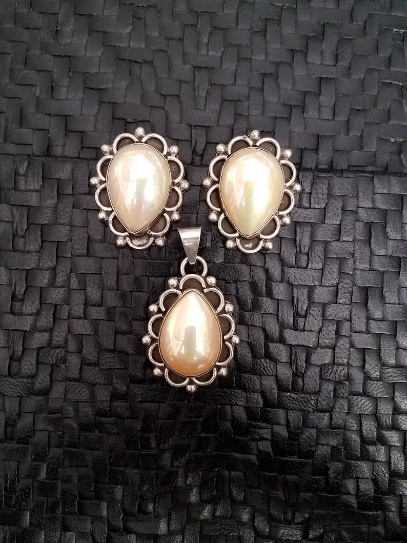 May include: A set of pearl earrings and a pendant necklace. The earrings and pendant feature a silver setting with a scalloped edge and a white pearl in the center.