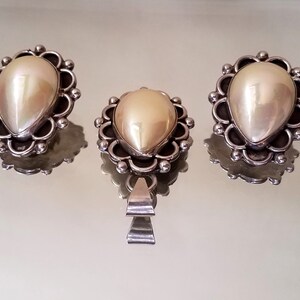 May include: A set of three silver earrings and a pendant featuring a pearlescent white stone in a decorative silver setting.