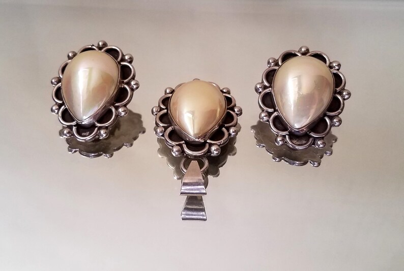 May include: A set of three silver earrings and a pendant featuring a pearlescent white stone in a decorative silver setting.