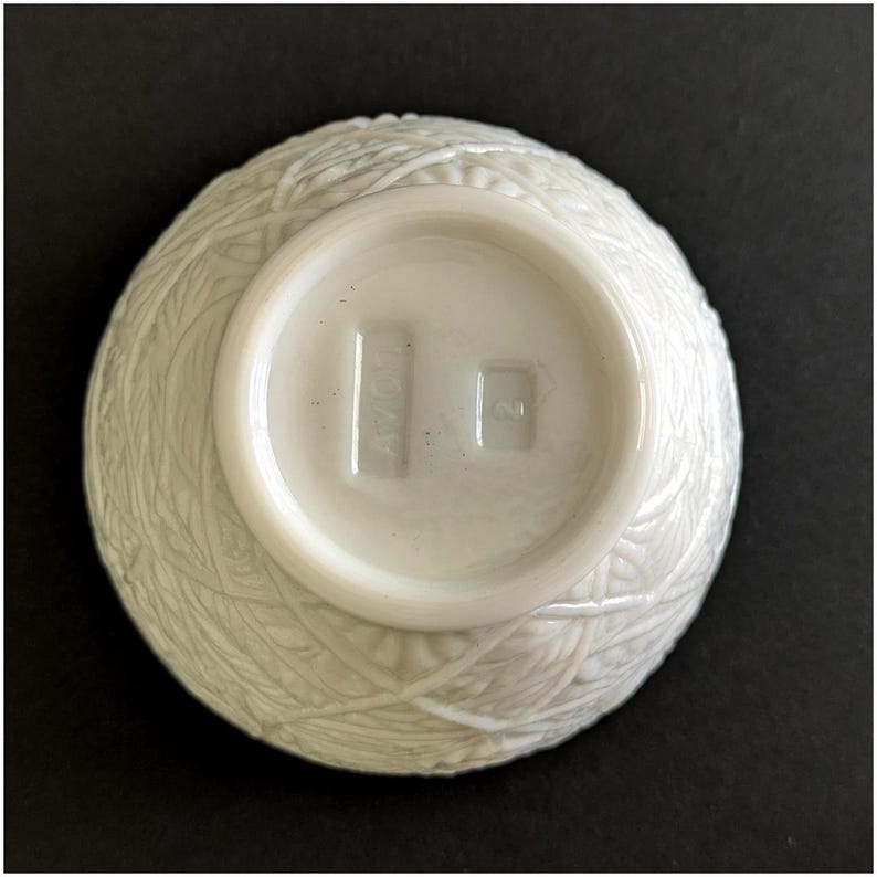 Puede incluir: Un cuenco de cer&aacute;mica blanca con un dise&ntilde;o texturizado y tejido en el exterior. La base del cuenco es lisa y presenta el texto "AVON" y un peque&ntilde;o cuadrado. El cuenco est&aacute; sobre un fondo oscuro.