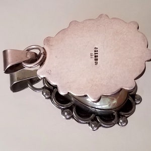 May include: Silver pendant with an ornate design and a silver cabochon stone. The back of the pendant is stamped with "925" and "MADE IN ITALY".