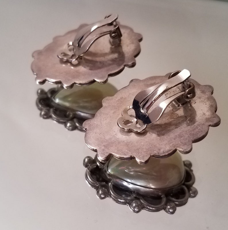 May include: A pair of silver tone clip-on earrings with a white iridescent stone set in a detailed silver tone frame.