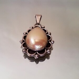 May include: A silver pendant with a pearlescent white teardrop-shaped stone set in a decorative silver frame.
