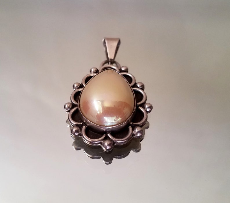 May include: A silver pendant with a pearlescent white teardrop-shaped stone set in a decorative silver frame.