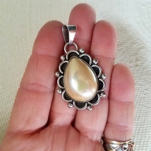 May include: A silver pendant with a pearlescent white teardrop-shaped stone set in a silver filigree design.