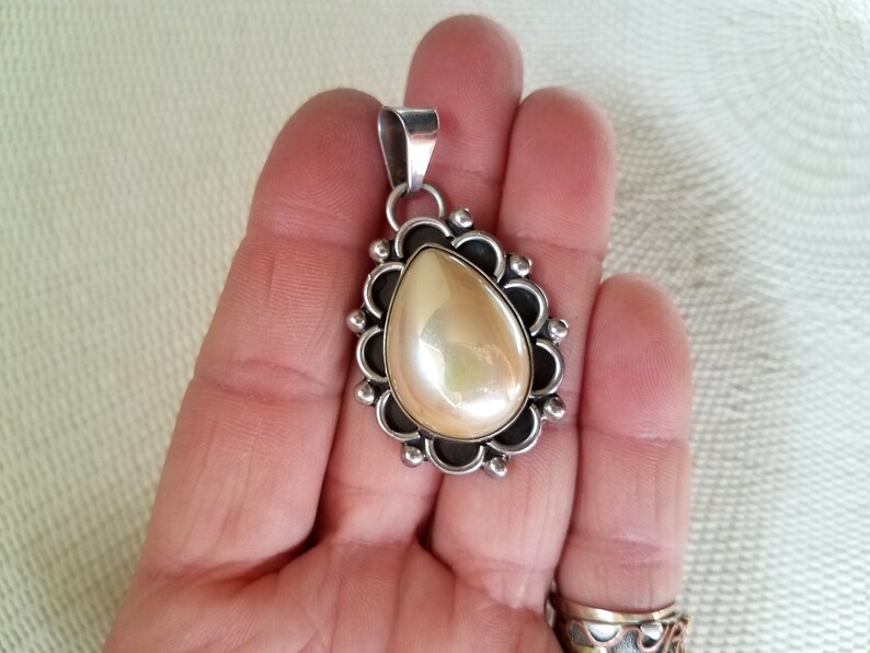 May include: A silver pendant with a pearlescent white teardrop-shaped stone set in a silver filigree design.
