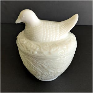 Puede incluir: Caja de baratijas blanca con forma de p&aacute;jaro sobre un nido. El p&aacute;jaro tiene una superficie texturizada y el nido presenta un patr&oacute;n de hojas. La caja est&aacute; hecha de un material brillante y opaco, de estilo vintage.