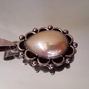 May include: A silver pendant with a large, pearlescent white gemstone set in a decorative, floral-shaped frame.